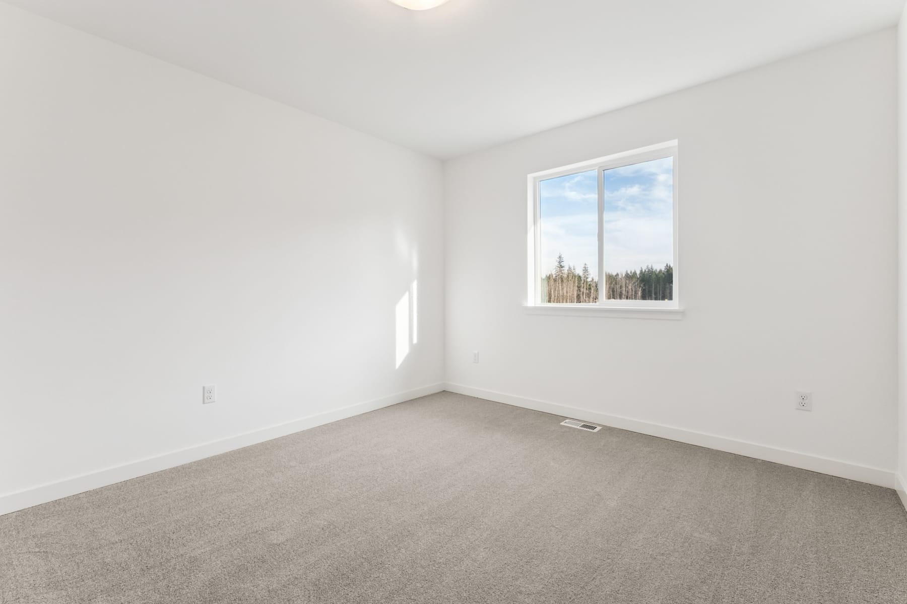 A bright, empty room with a large window overlooking a forested landscape.