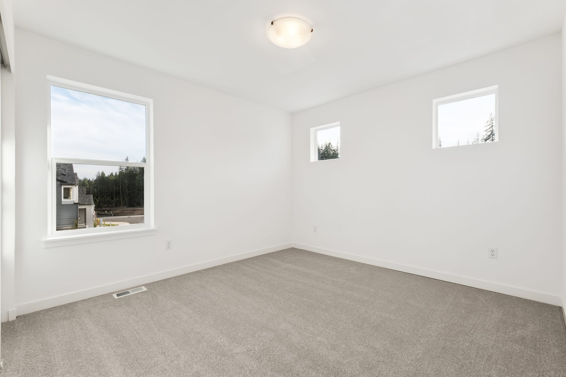 A bright, empty room with white walls, a light fixture, and a window overlooking a forested landscape.