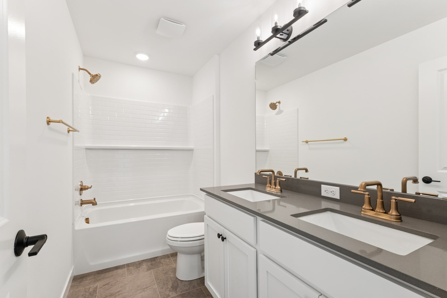 A modern, minimalist bathroom with a white vanity, a large mirror, and various gold-toned fixtures and hardware.