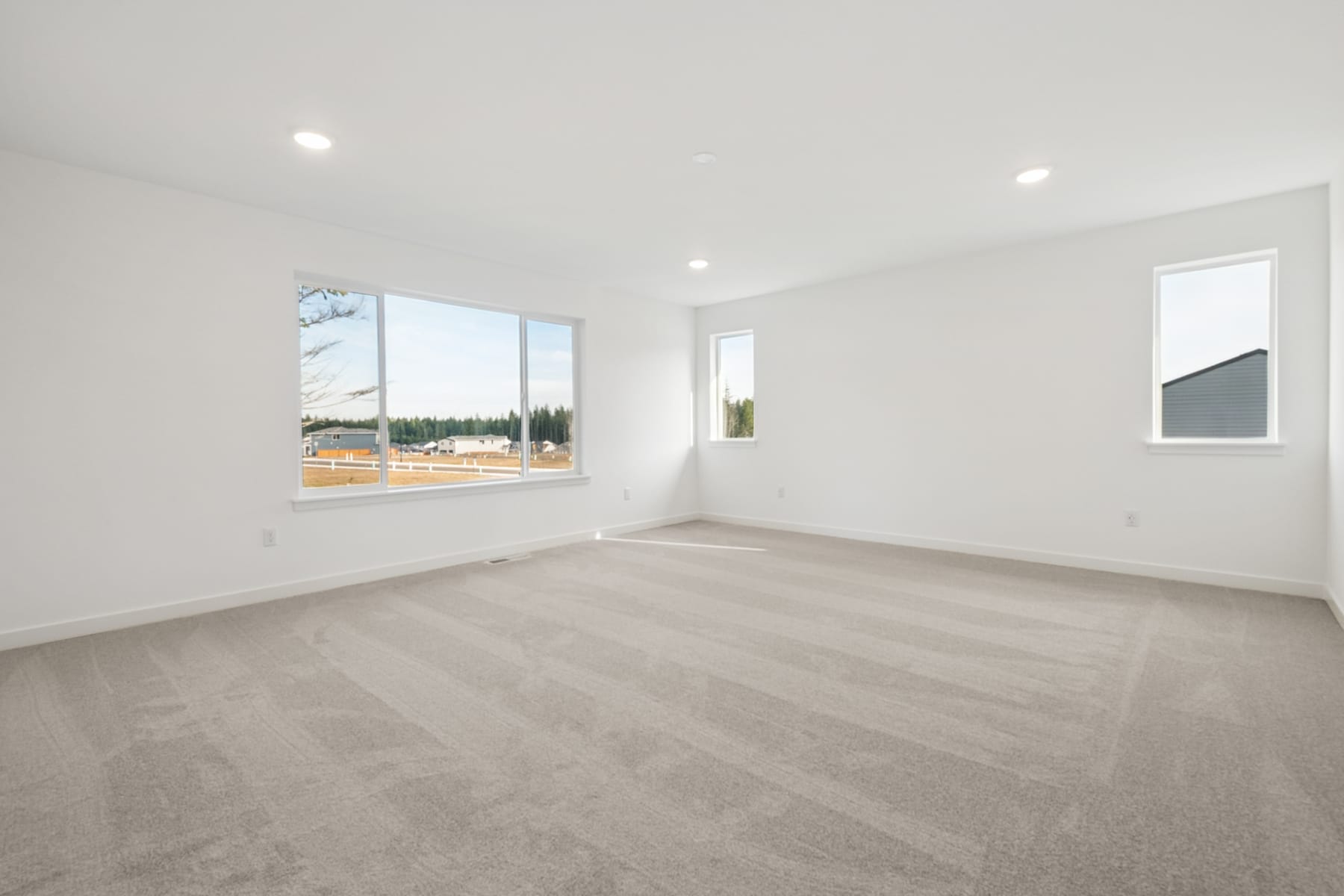 A spacious, bright room with large windows overlooking a forested landscape, featuring a clean, minimalist design with hardwood floors.