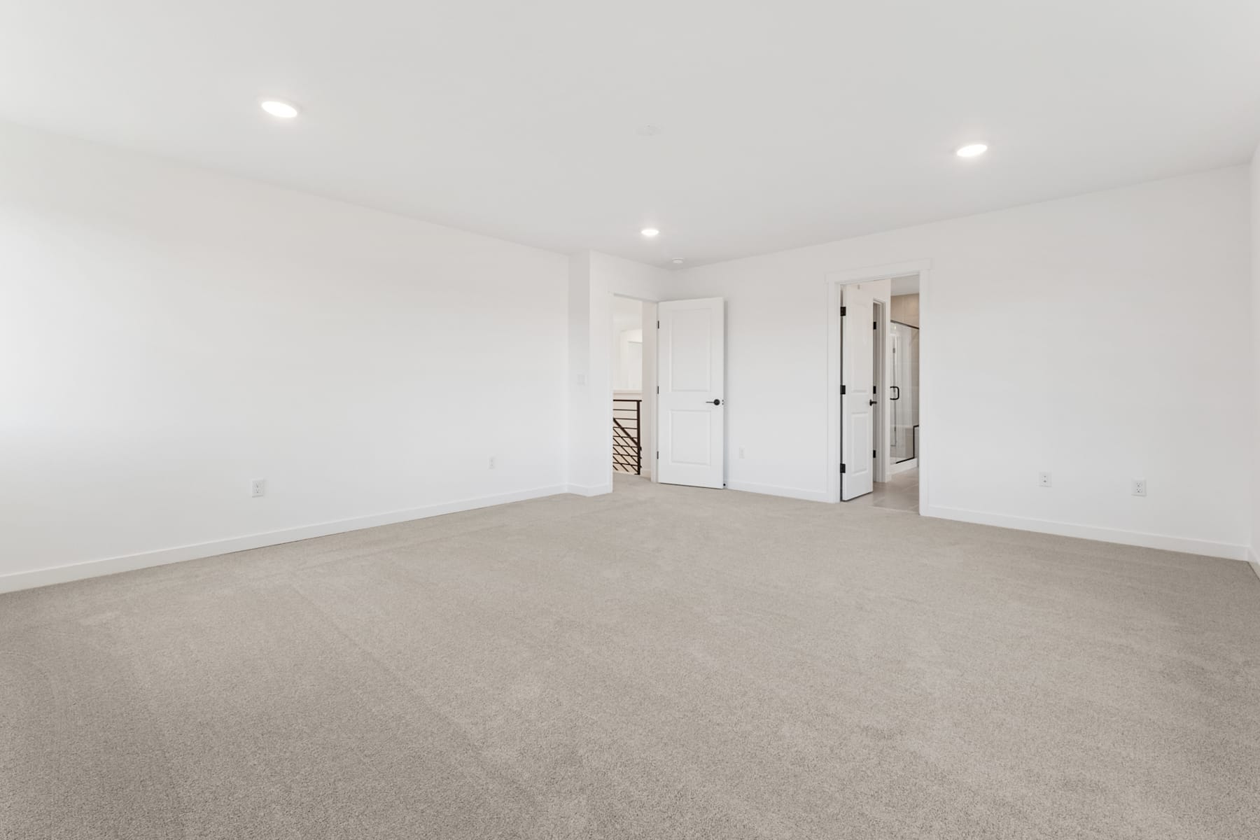 A spacious, minimalist room with white walls, a carpeted floor, and several doors leading to other areas.