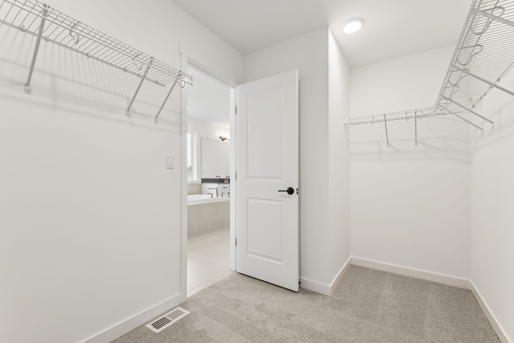 A bright, minimalist laundry room with white walls, a closed door, and wire shelving units on the walls.