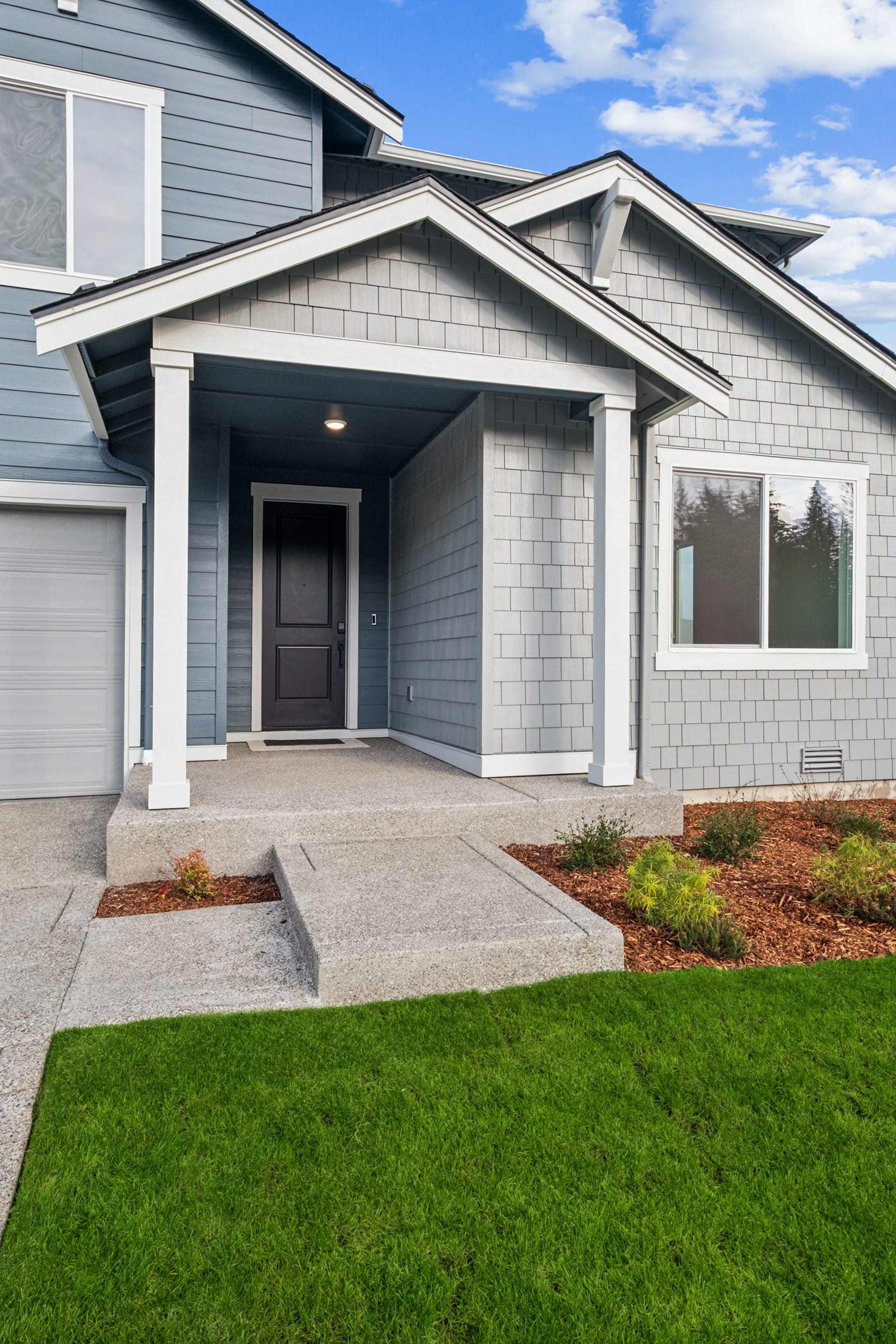 A modern, two-story house with a covered entryway, gray siding, and a well-manicured lawn in the foreground.