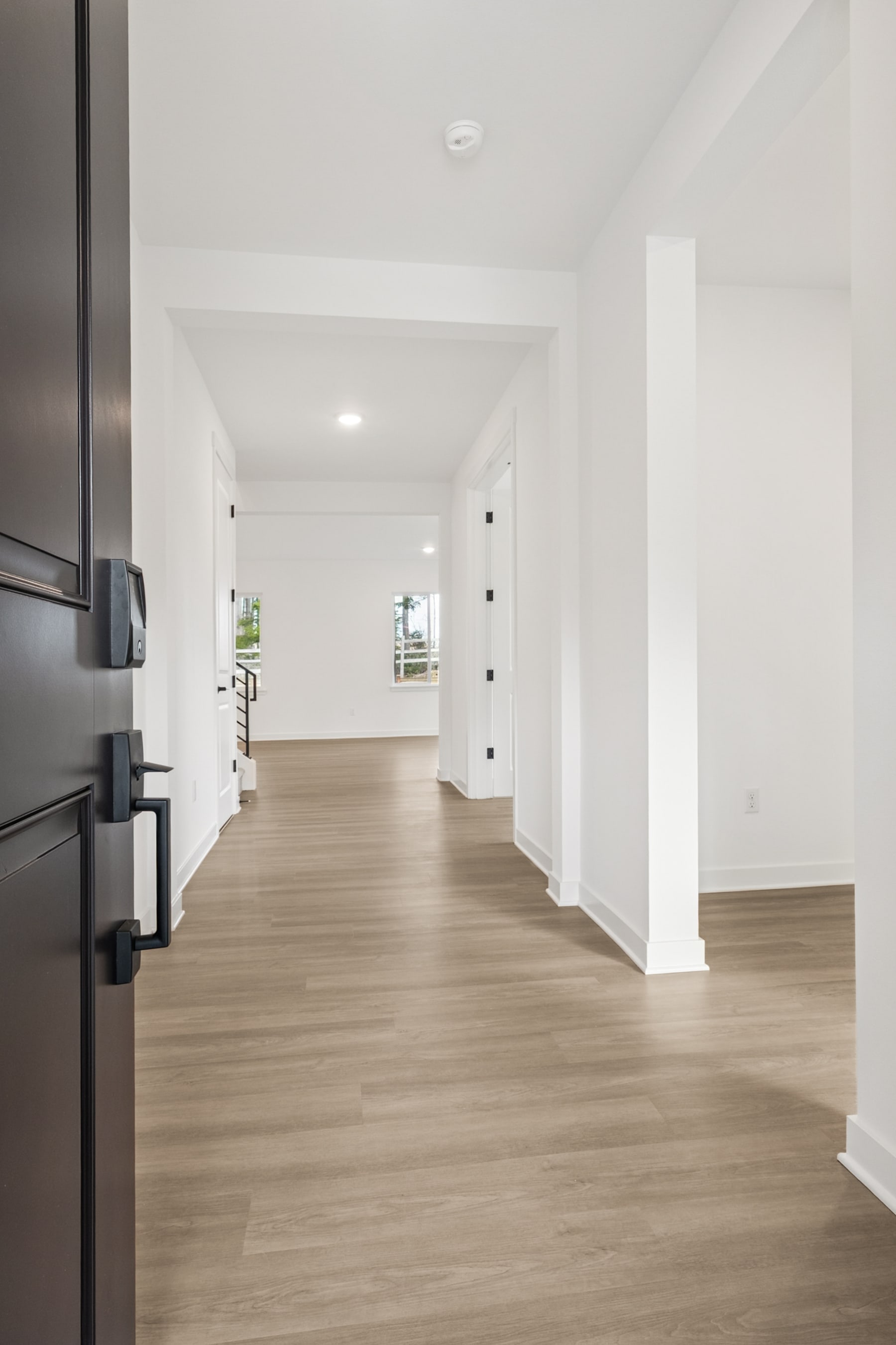 A spacious, well-lit hallway with a wooden floor and white walls, leading to an open space beyond.