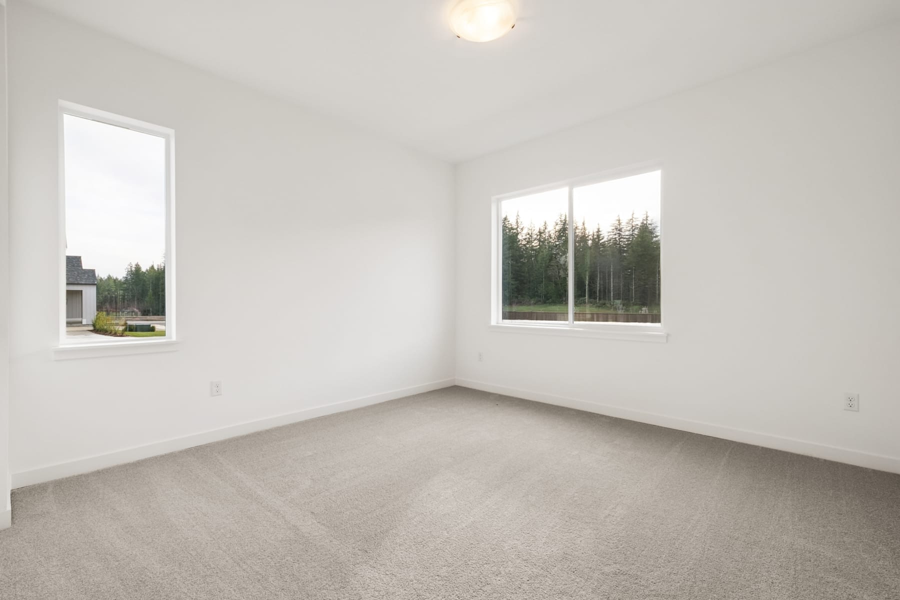 A bright, minimalist room with large windows overlooking a forested landscape.