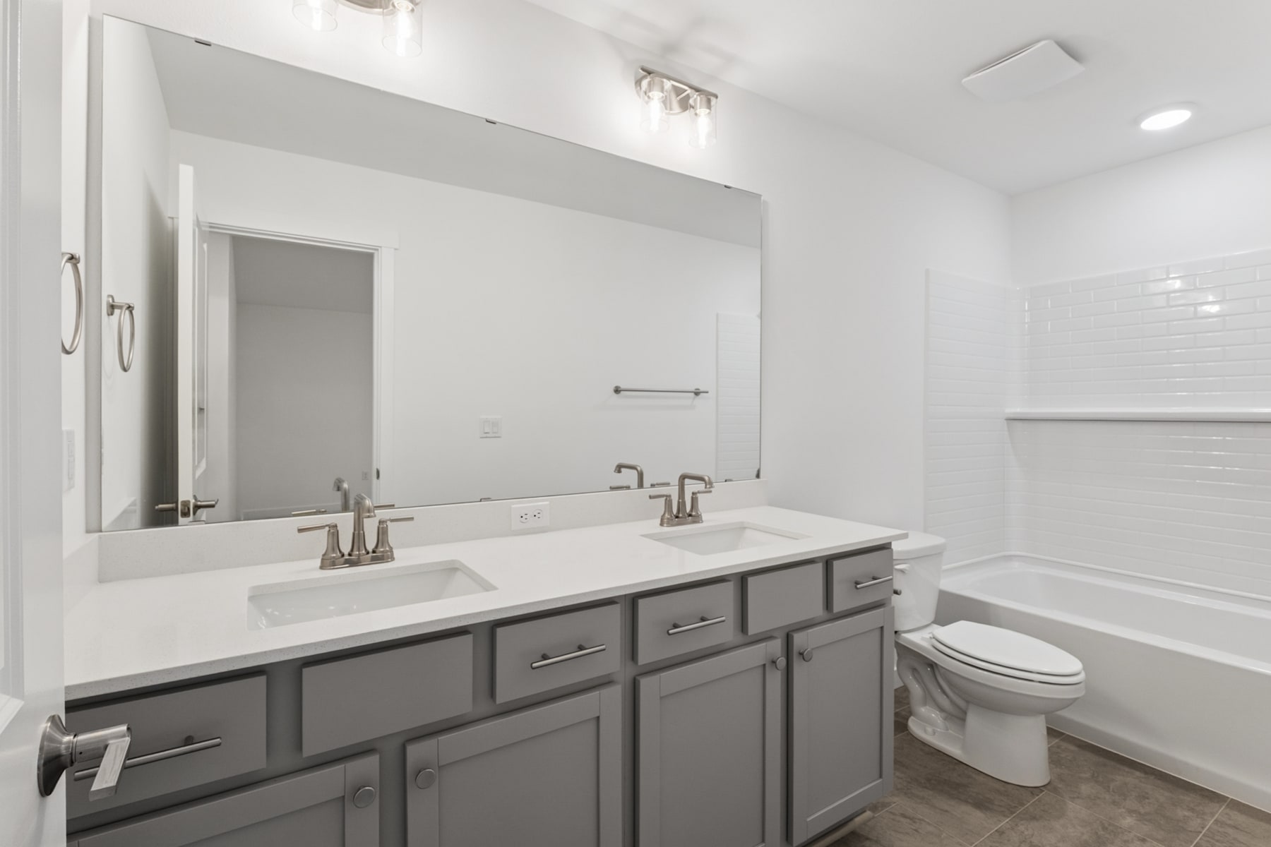 A modern, minimalist bathroom with a large vanity, double sinks, and a toilet in the background, all in a clean, white and gray color scheme.