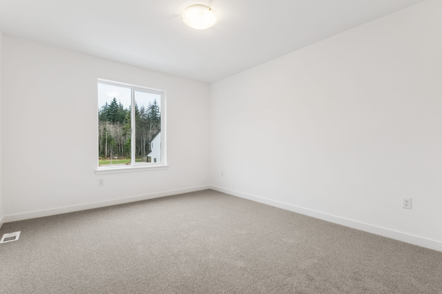 A bright, empty room with a large window overlooking a forested landscape.