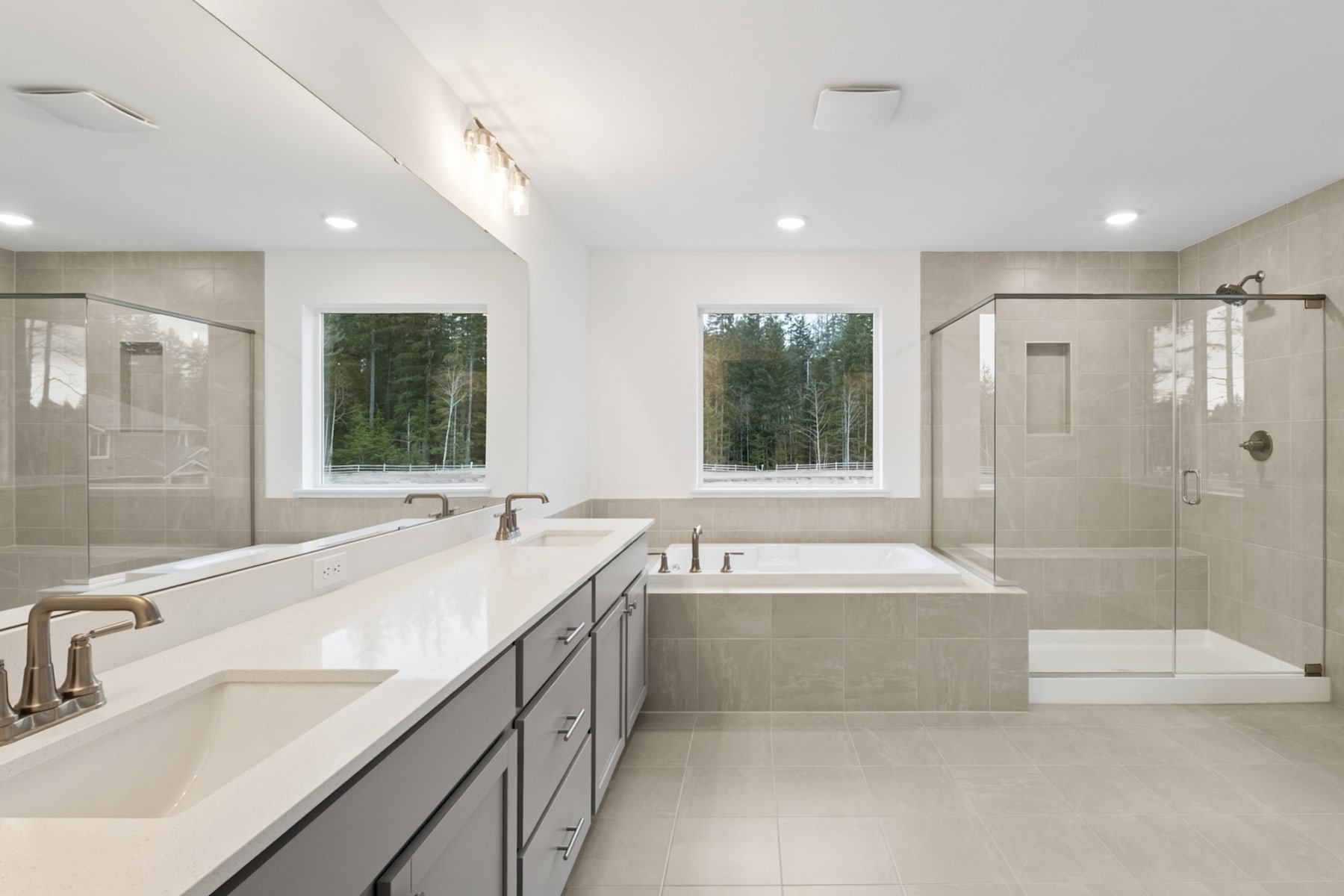 A spacious and modern bathroom with a large vanity, a freestanding bathtub, and large windows overlooking a forested landscape.