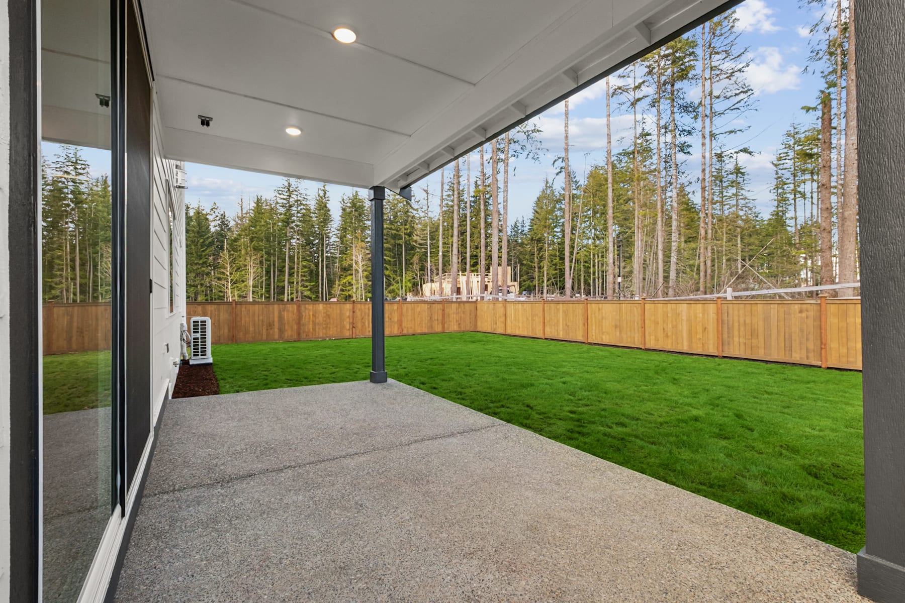 A covered patio with a lush green lawn and a backdrop of a dense forest, creating a serene and peaceful outdoor living space.