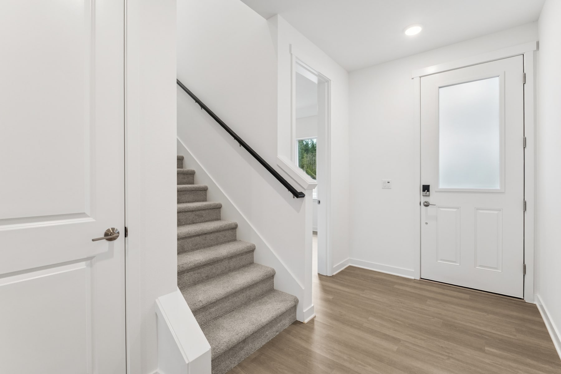 A bright and spacious entryway with a staircase leading upstairs, a white door, and a hardwood floor.