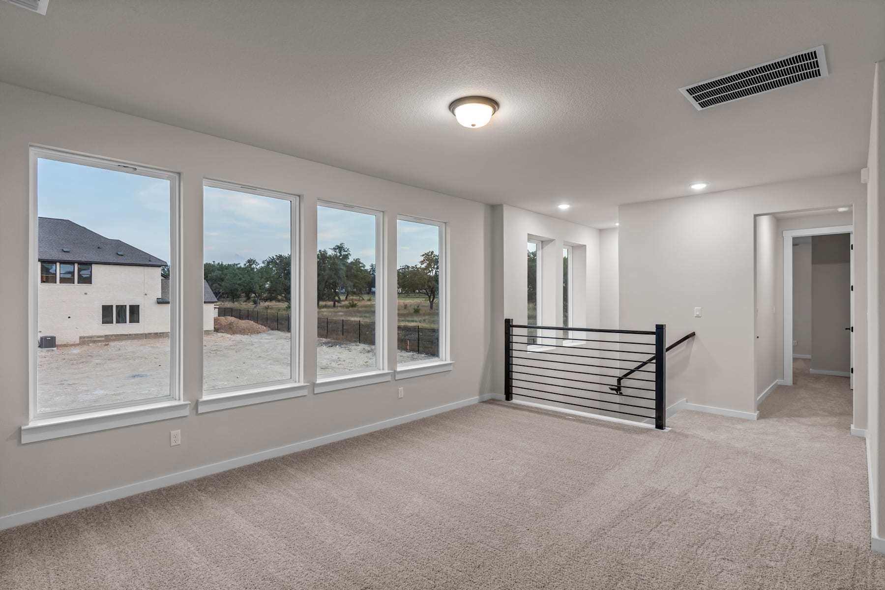 A spacious, well-lit room with large windows overlooking a scenic outdoor landscape, featuring a staircase and hardwood flooring.