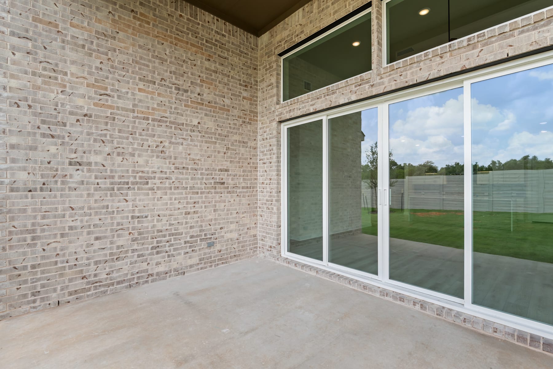 A spacious patio with a brick wall and large glass windows overlooking a grassy outdoor area.