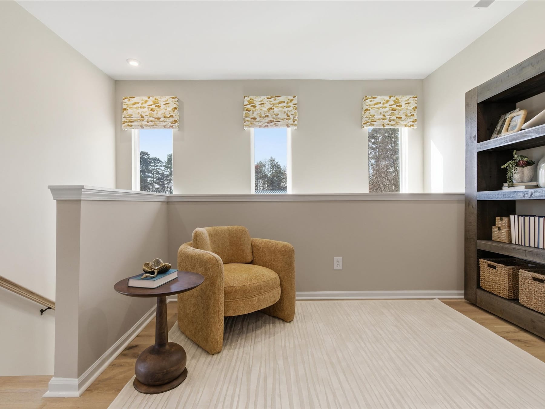 A cozy living room with a comfortable yellow armchair, a side table, and built-in shelves displaying various decorative items, all set against a backdrop of large windows offering a scenic outdoor view.