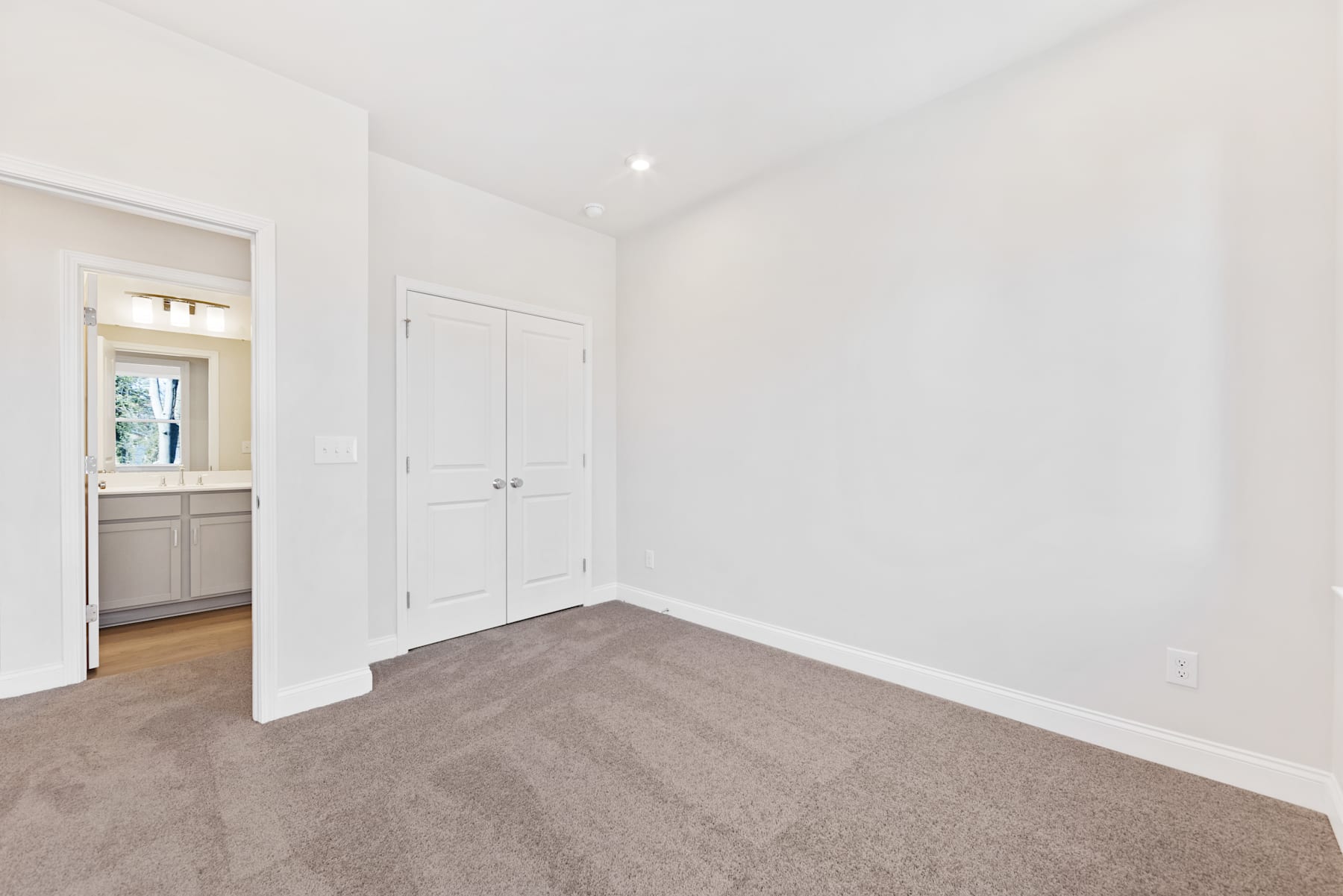 A spacious, well-lit room with white walls, a wooden floor, and a closed door leading to another room.
