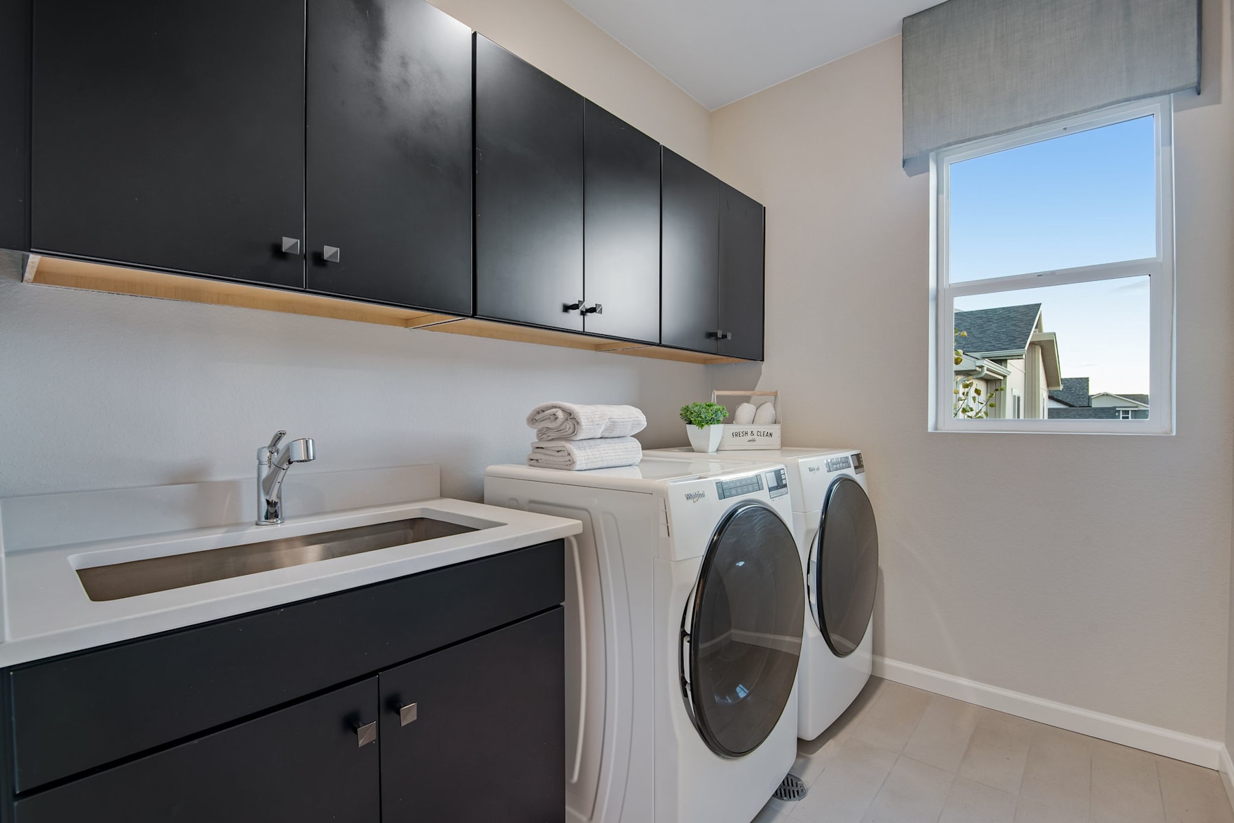 A modern and well-equipped laundry room with black cabinets, a sink, and a pair of front-loading washing machines against a bright, airy background.