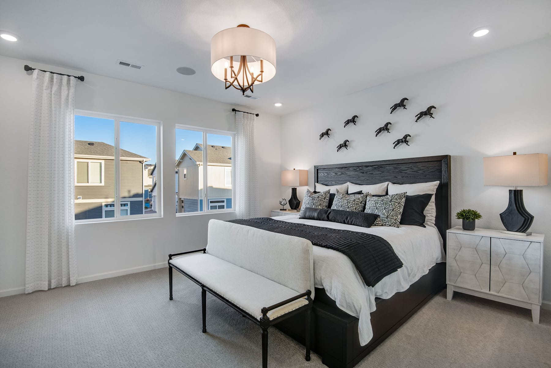 A modern and stylish bedroom with a large bed, a chandelier, and decorative wall art featuring silhouettes of birds.
