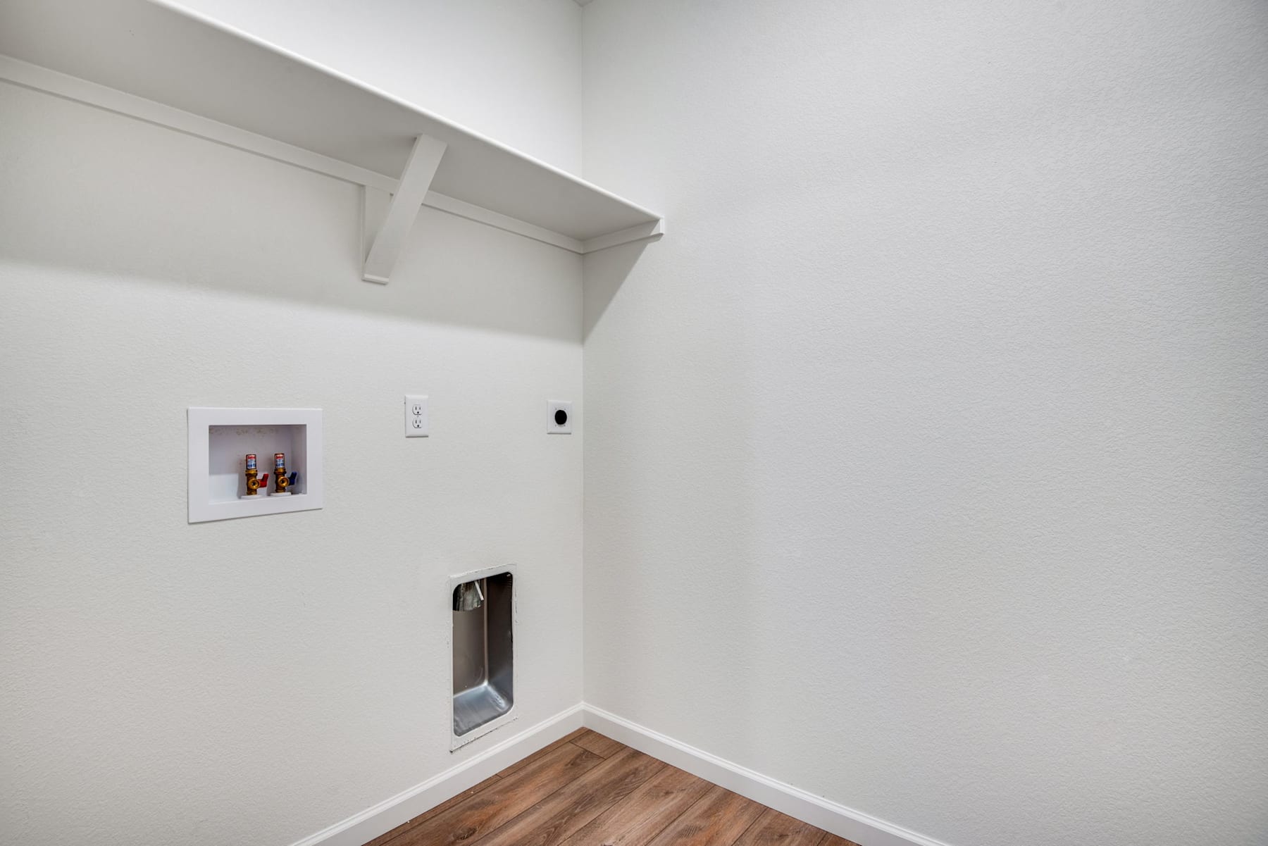 A white-walled room with a wooden floor, a small niche in the wall, and a door visible in the corner.