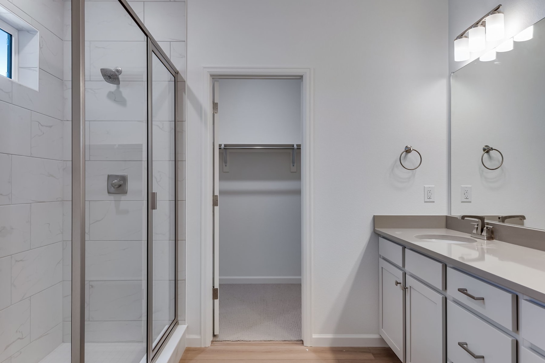 A modern bathroom with a glass shower enclosure, a vanity with a countertop, and a closet or storage space visible in the background.