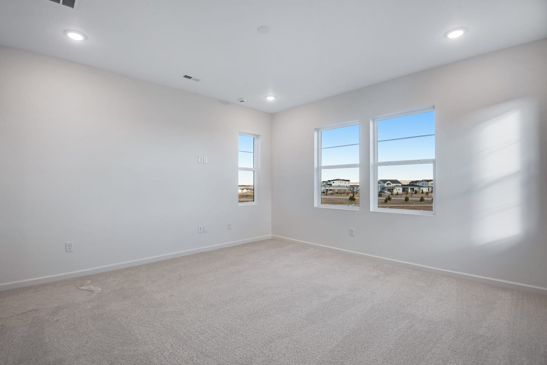 A spacious, well-lit room with large windows overlooking a residential area in the background.