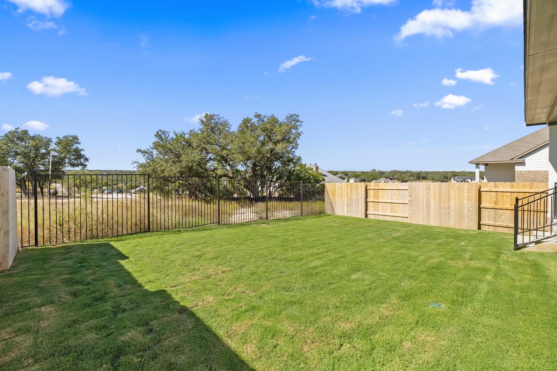 A well-manicured lawn surrounded by a wooden fence, with lush trees and a clear blue sky in the background.