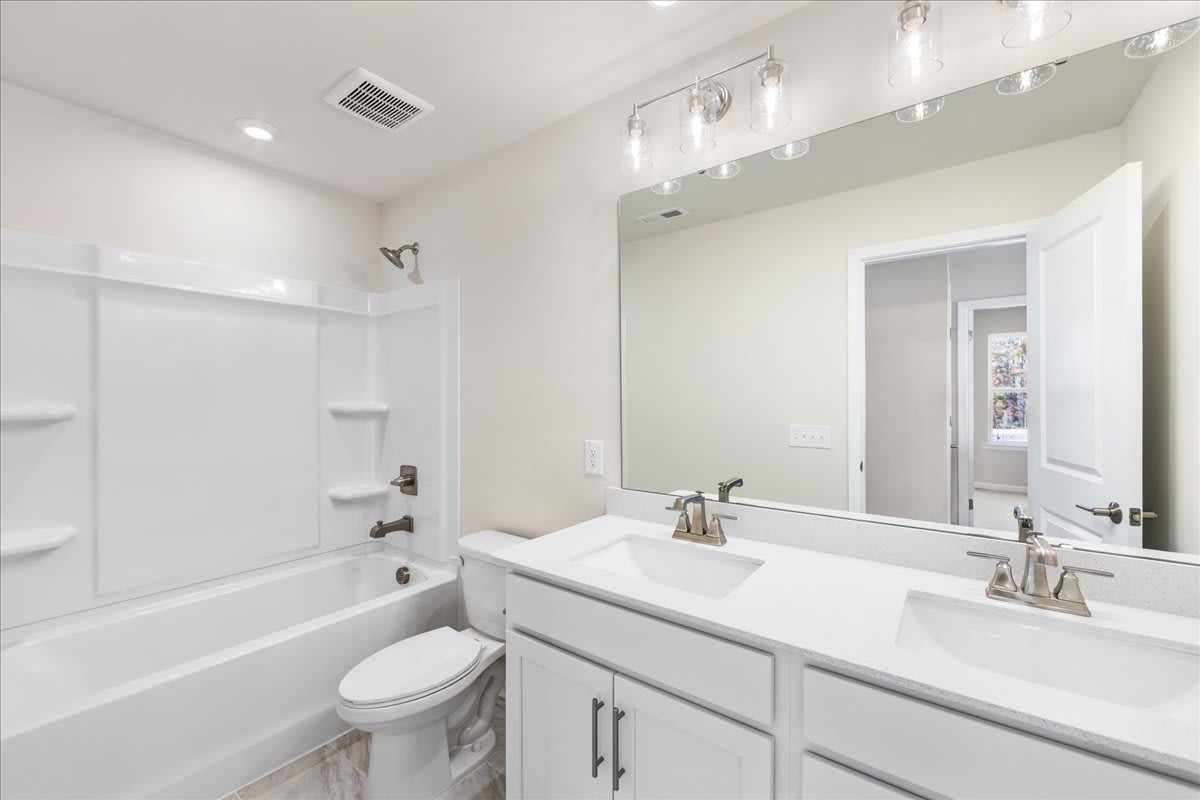 A modern, well-lit bathroom with a vanity, sink, and mirror, as well as a bathtub and toilet visible in the background.