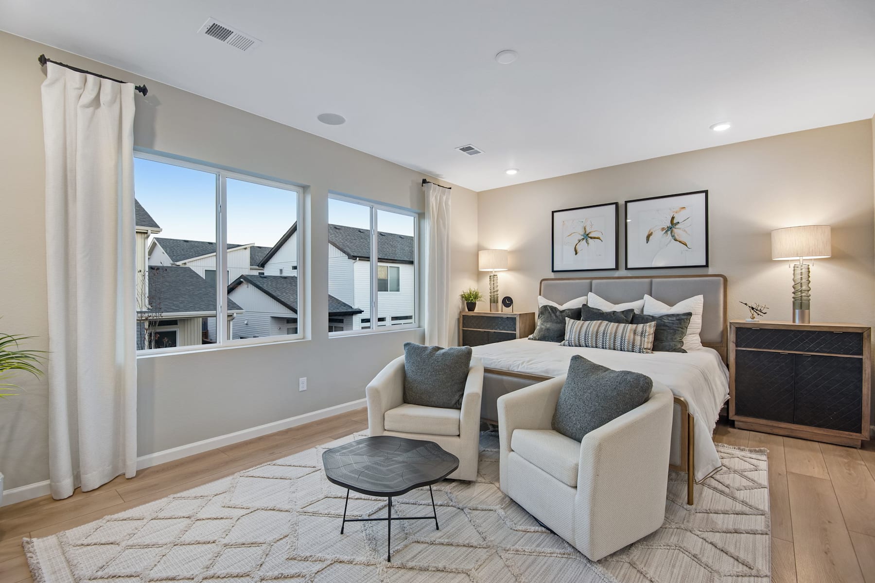 A cozy and well-furnished bedroom with large windows, neutral-toned decor, and a comfortable seating area in the foreground.