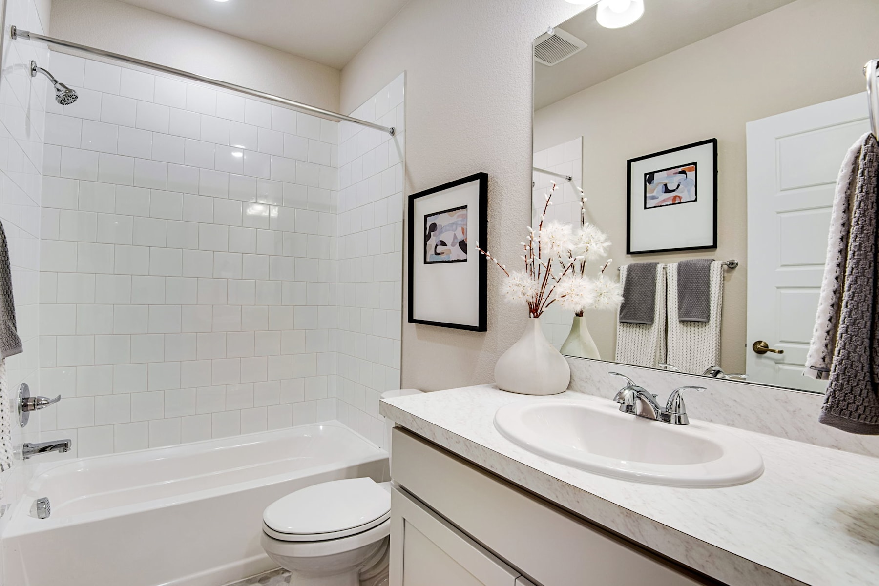 A modern and minimalist bathroom with a white vanity, a large mirror, and framed artwork on the walls.