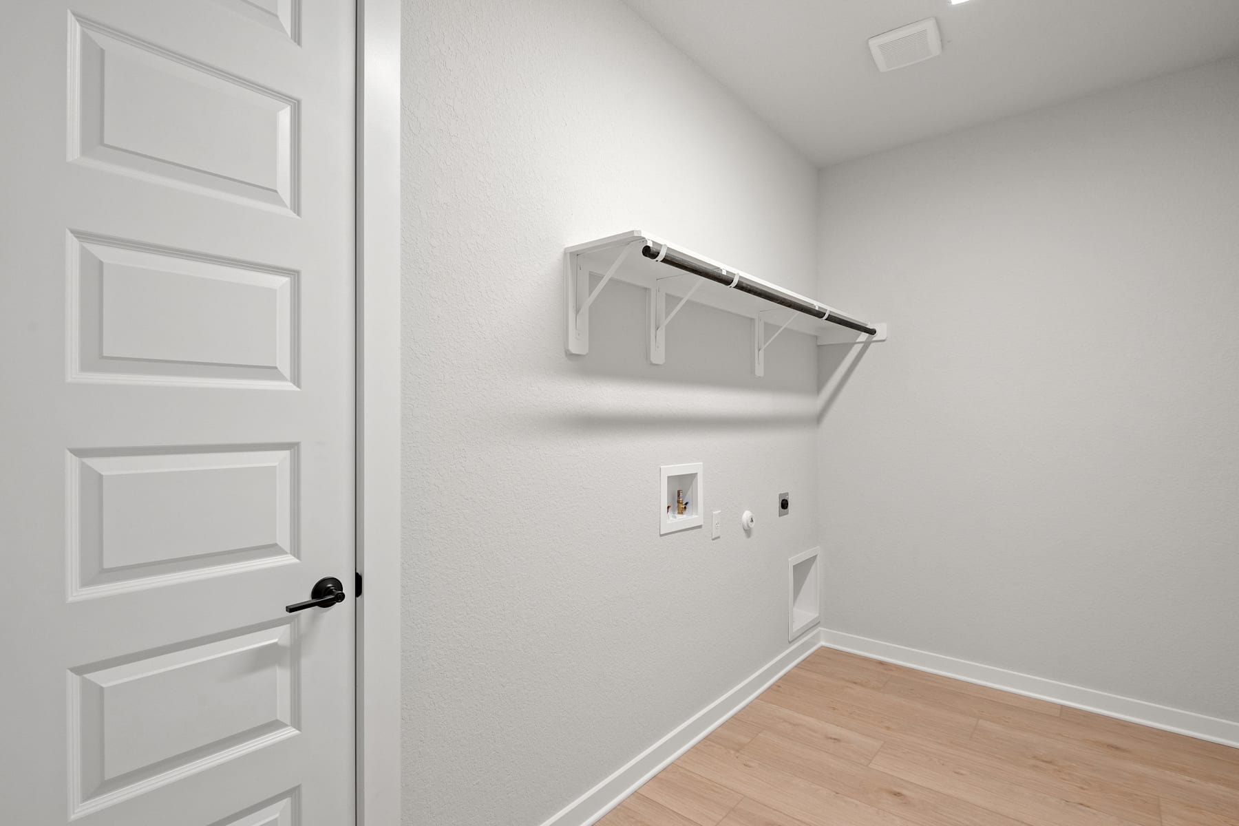A simple, minimalist room with a white door, a wall-mounted shelf, and a light-colored wooden floor.
