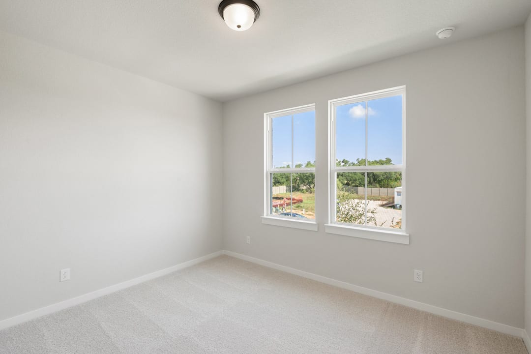 A bright, empty room with large windows overlooking a lush, green outdoor landscape.