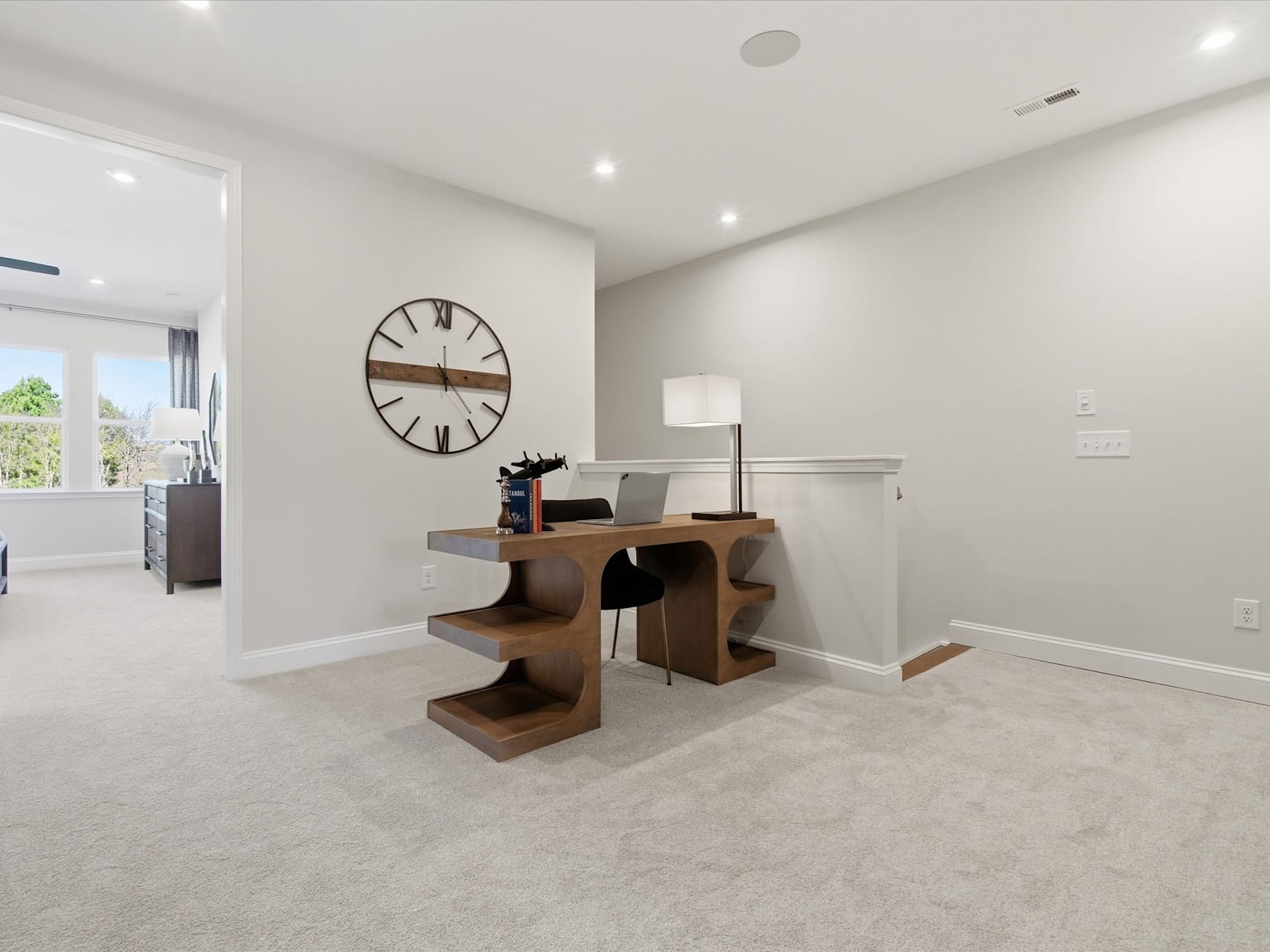 A modern and minimalist home office space with a wooden desk, a large wall clock, and a clean, bright interior.