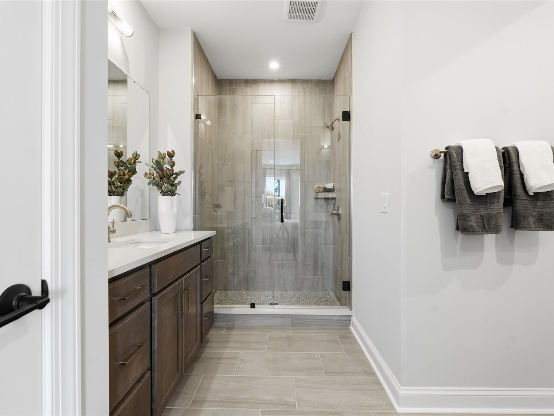 A modern and spacious bathroom with a vanity, shower, and neutral-toned tiles covering the floor and walls.