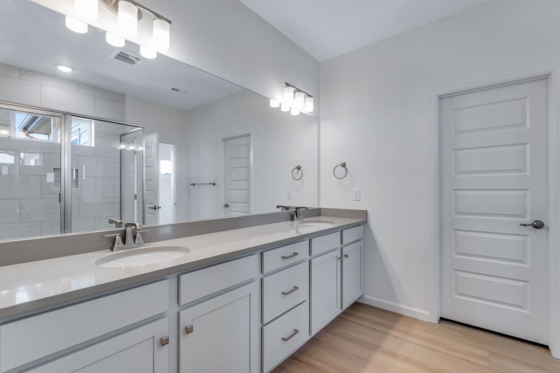 A modern and well-lit bathroom with a double vanity, a large mirror, and a glass-enclosed shower area.