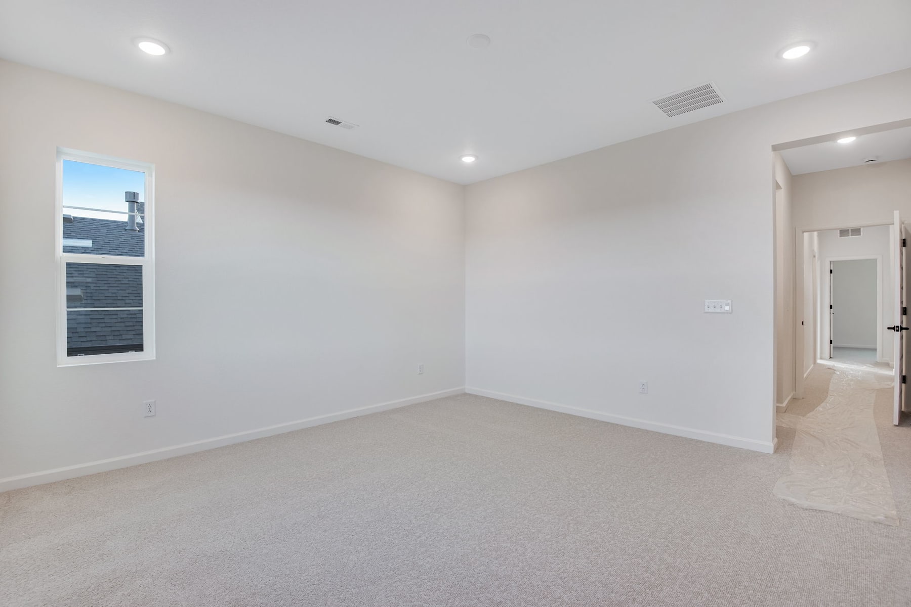 An empty, well-lit room with white walls, a carpeted floor, and recessed lighting fixtures.