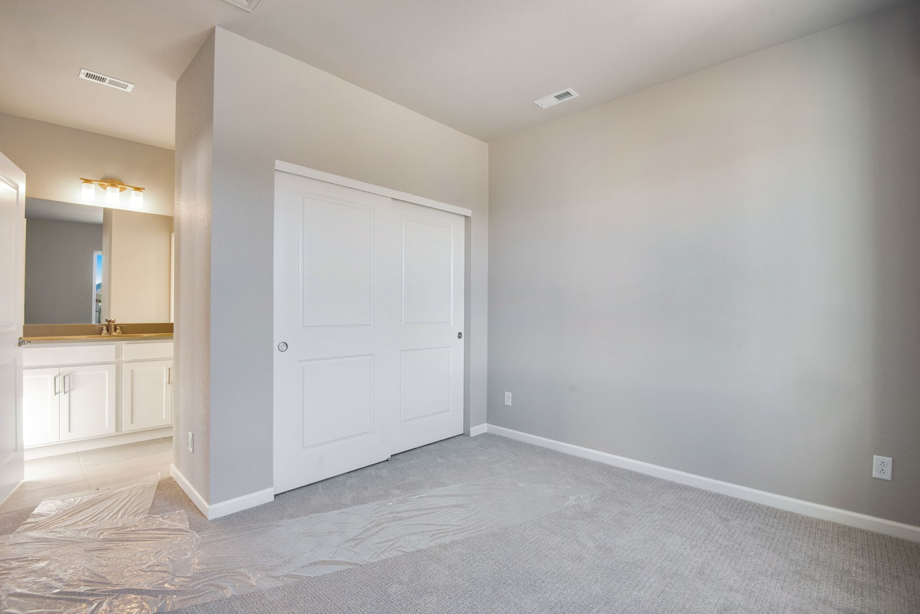 A spacious, minimalist bedroom with a white door, neutral-colored walls, and a carpeted floor.