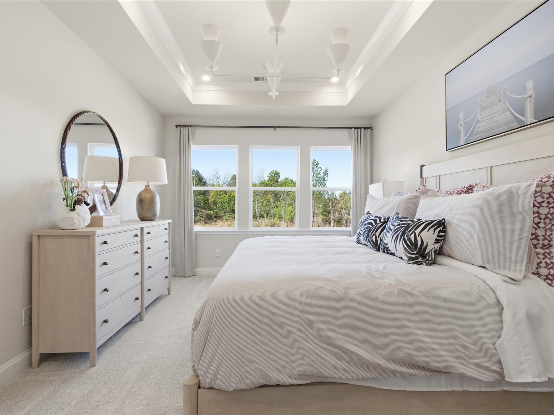 A spacious and well-lit bedroom with a large bed, dresser, and mirror, overlooking a scenic outdoor view through the window.