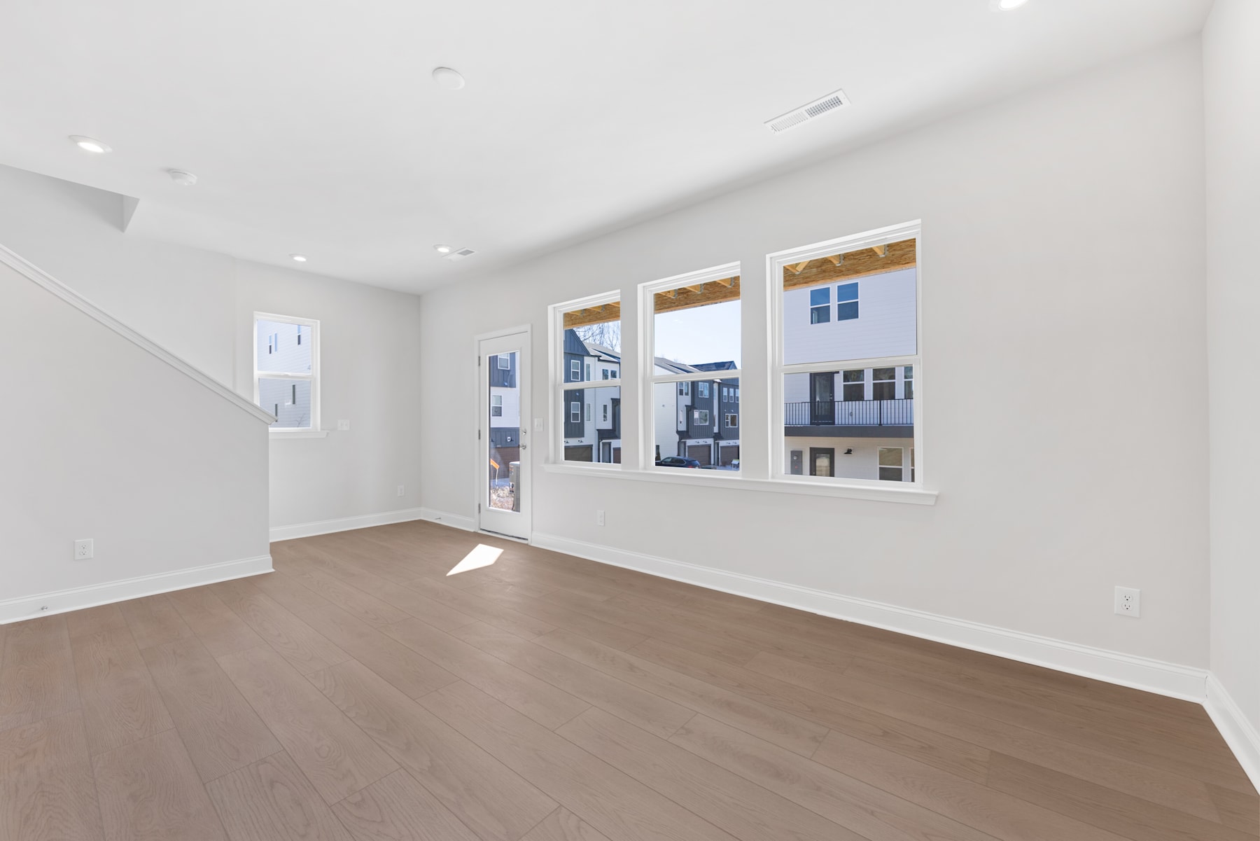 A spacious, well-lit room with large windows overlooking a residential area, featuring a hardwood floor and a minimalist, modern design.