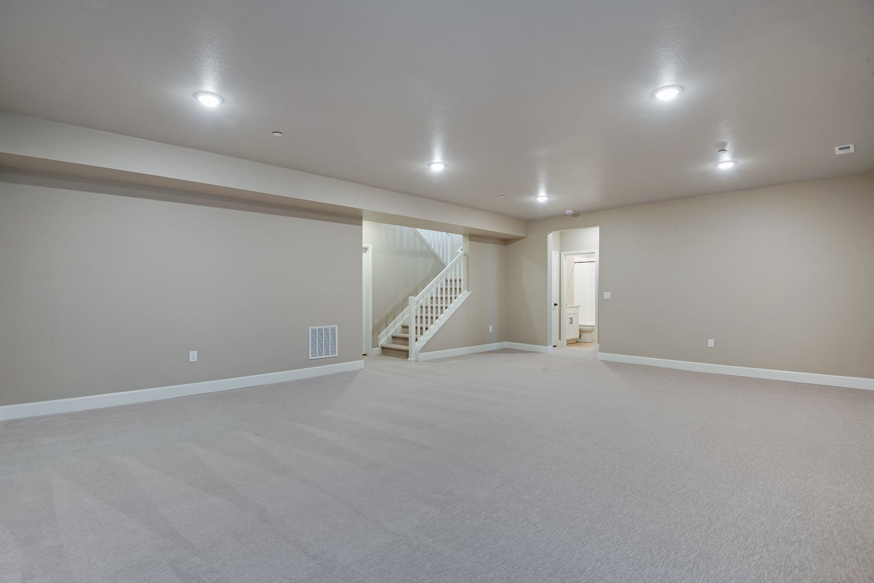 A spacious, well-lit room with a staircase leading to an upper level, featuring a clean and minimalist design with white walls and floors.