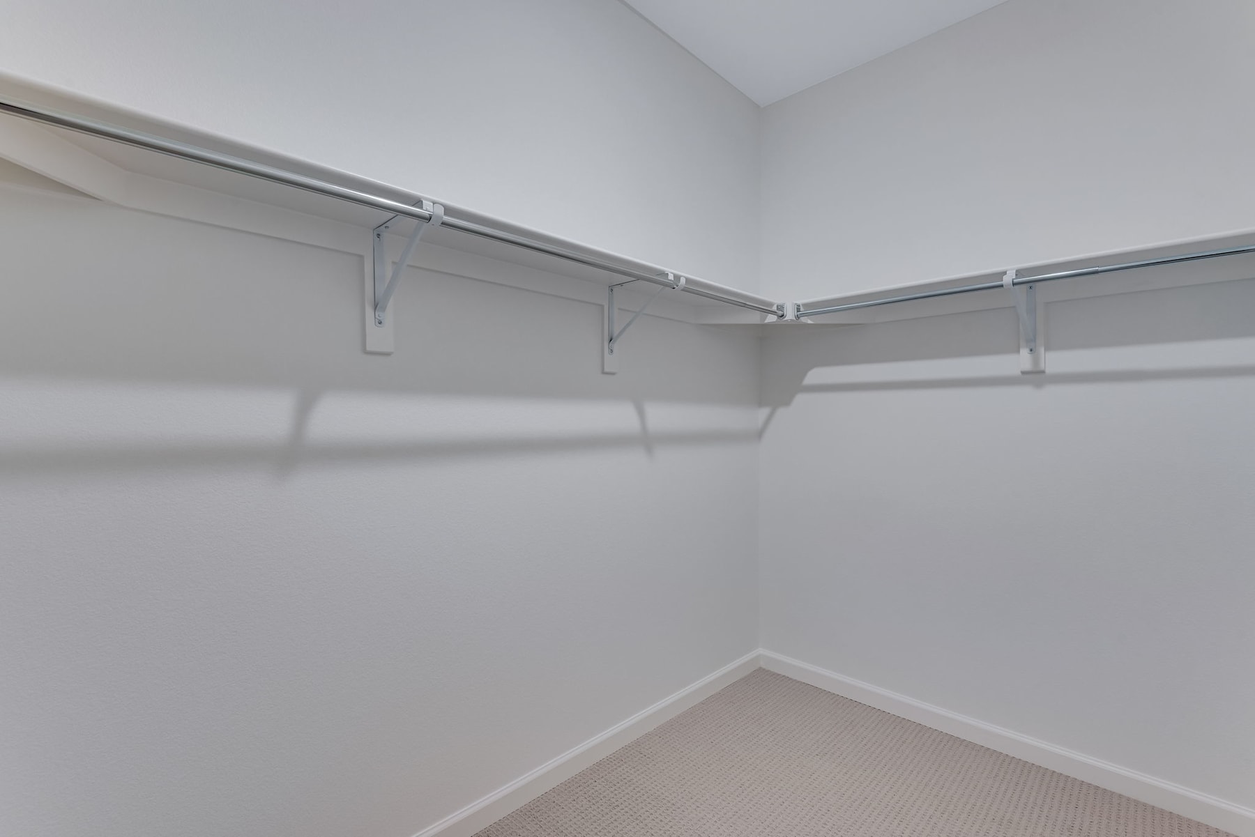 A white, empty closet with a metal rod and hangers installed along the walls, creating a simple and organized storage space.