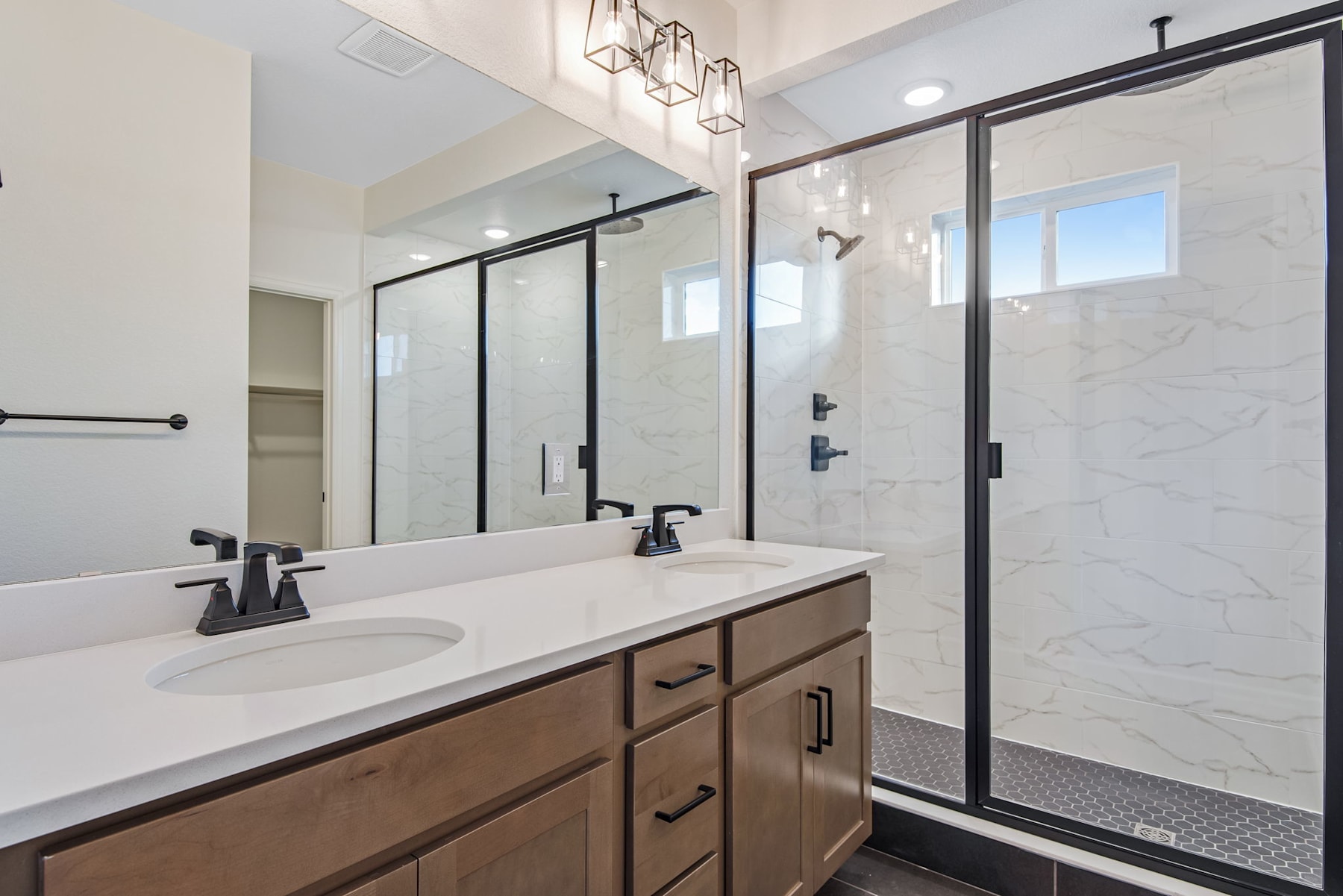 A modern and spacious bathroom with a vanity, double sinks, and a large glass-enclosed shower area, featuring sleek black hardware and fixtures.