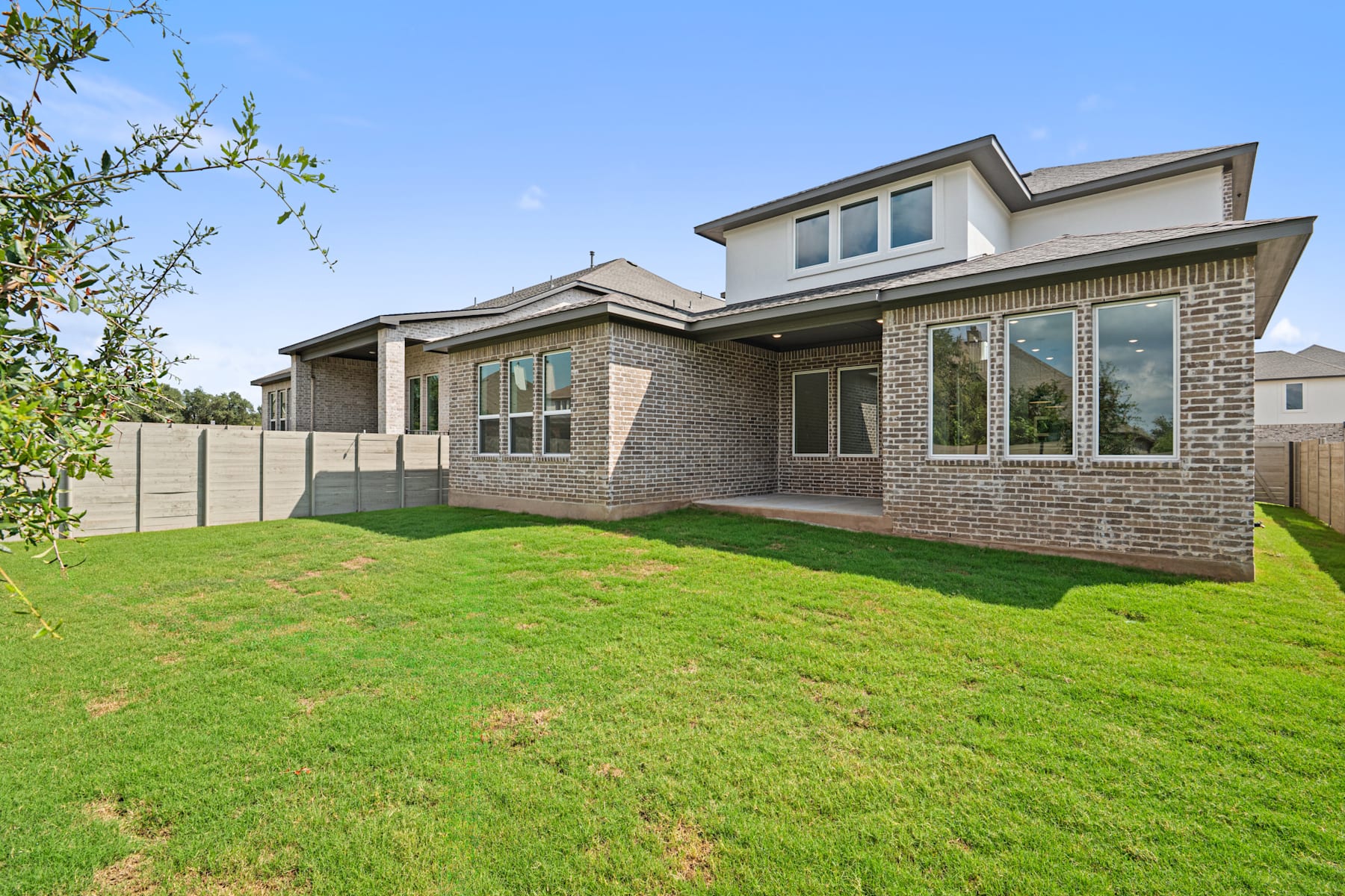 A well-maintained brick house with a lush green lawn in the foreground, surrounded by trees and a clear blue sky in the background.