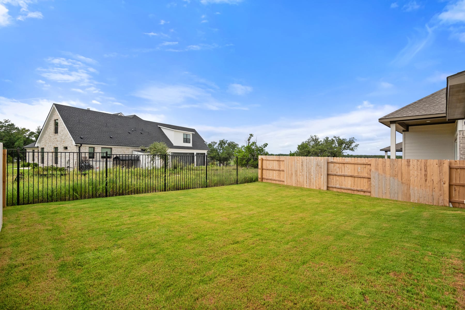 A well-manicured lawn surrounded by a wooden fence, with a residential neighborhood visible in the background under a clear blue sky.