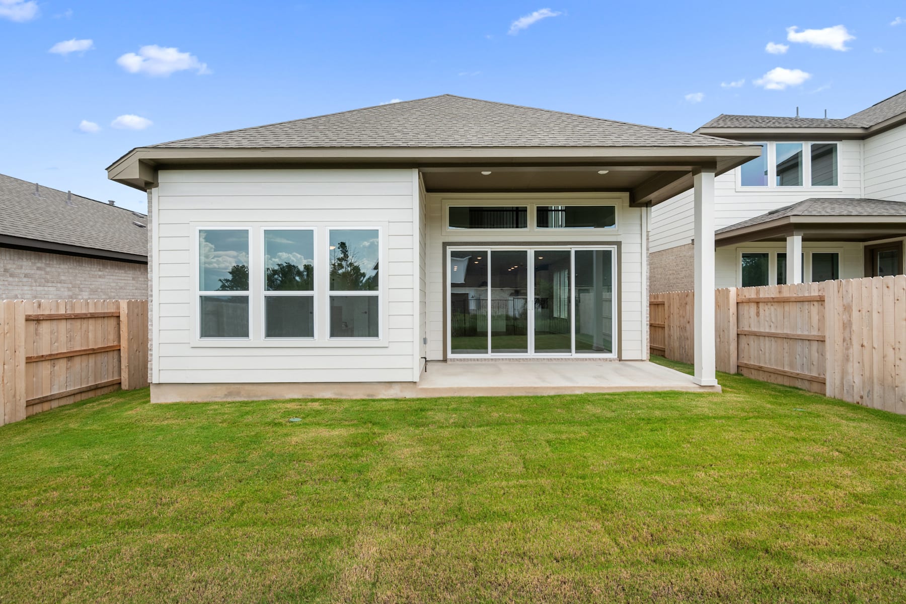 A modern, single-story house with a covered porch and large windows stands in a grassy yard, surrounded by other residential buildings.