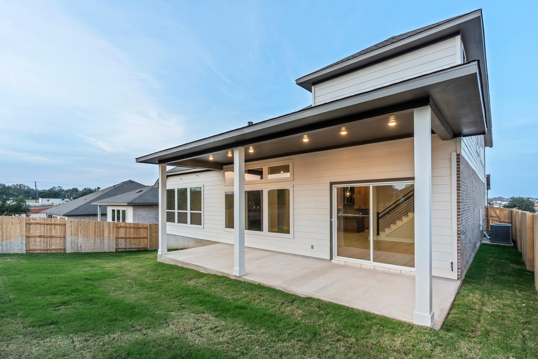 A modern, single-story house with a covered patio and a grassy yard in the foreground, set against a clear sky in the background.
