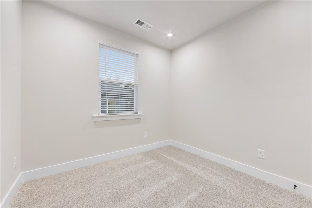 A bright, empty room with a window and white walls, featuring a carpeted floor.