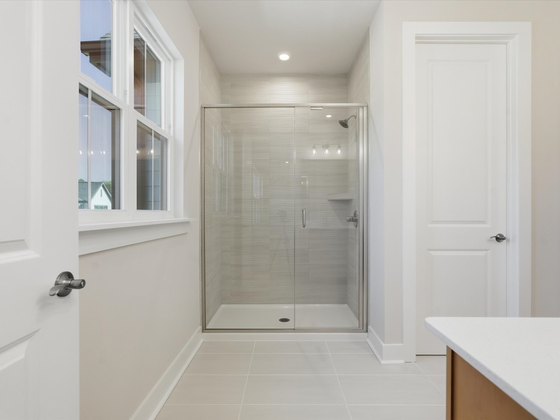 A bright and spacious bathroom with a glass-enclosed shower, white walls, and a wooden vanity.
