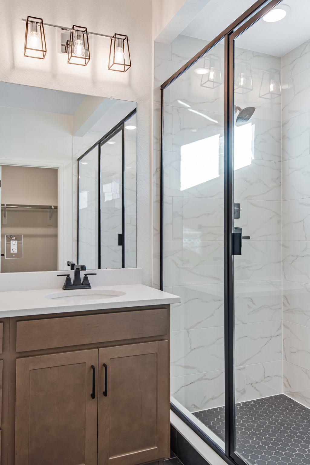 A modern bathroom with a vanity, mirror, and glass shower enclosure, illuminated by stylish pendant lights.