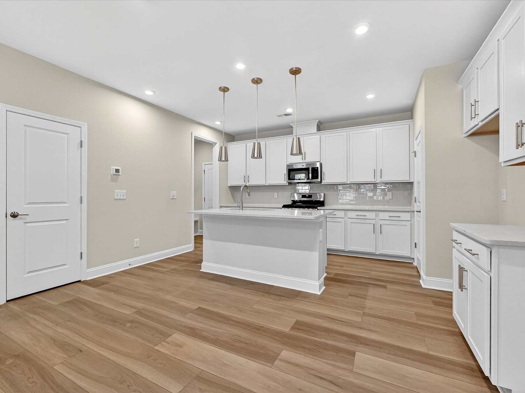 A modern, open-concept kitchen with white cabinets, stainless steel appliances, and hardwood floors, creating a bright and spacious living environment.