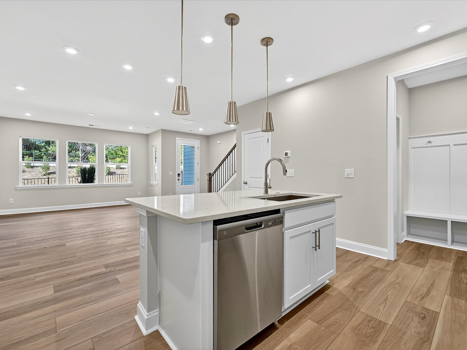 A modern, open-concept kitchen with white cabinets, a large island, and pendant lighting fixtures, set against a backdrop of hardwood floors and a staircase leading to an upper level.