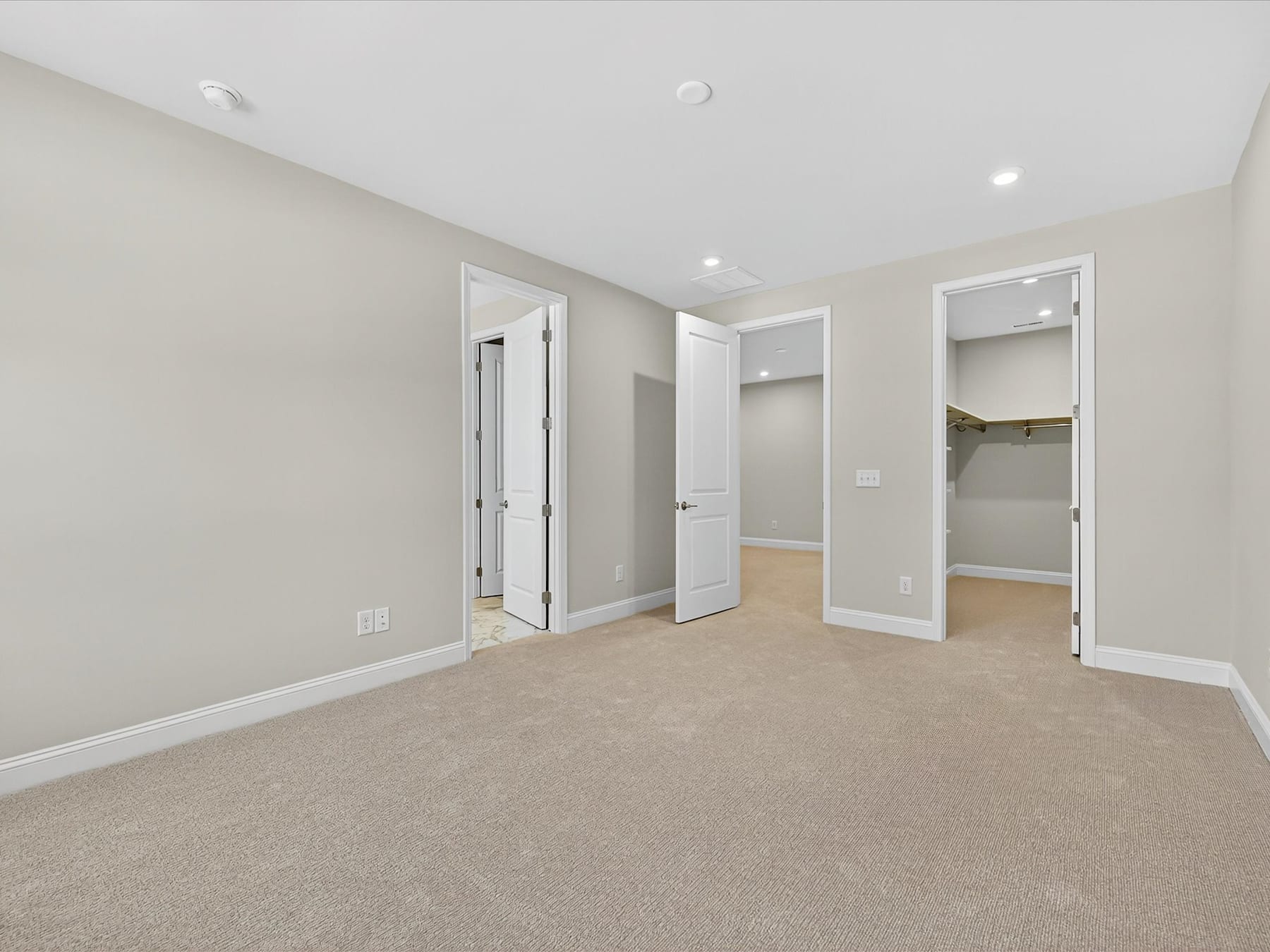A spacious, well-lit room with beige walls, white doors, and a carpeted floor, creating a clean and inviting atmosphere.