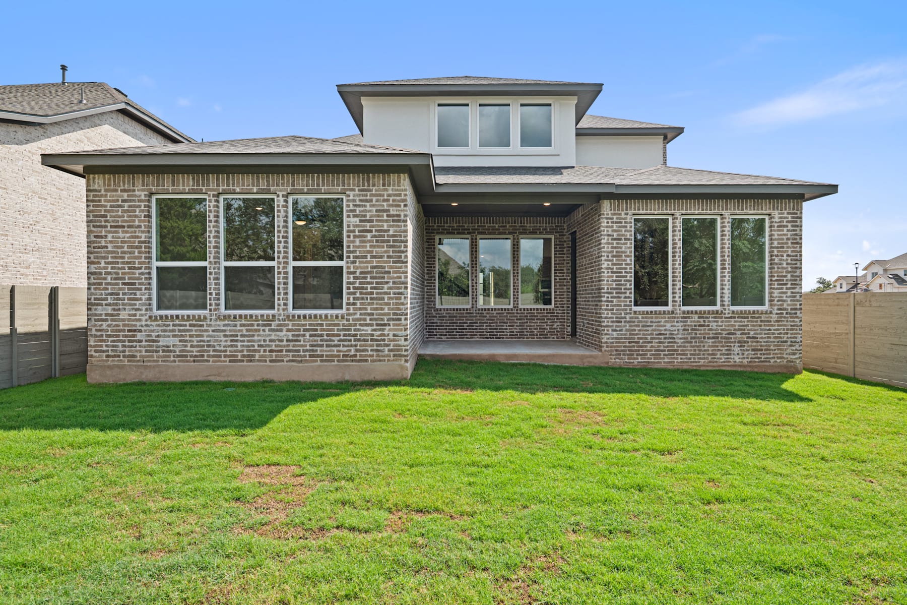 A modern two-story brick house with large windows and a well-manicured lawn in the foreground, set against a clear blue sky.
